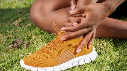 A person gently holds their foot while seated on grass, showcasing the relevance of podiatry in everyday life.